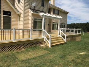 A pressure treated deck with white vinyl railings and black tubular balusters and a trellis located in Kintnersville PA.
